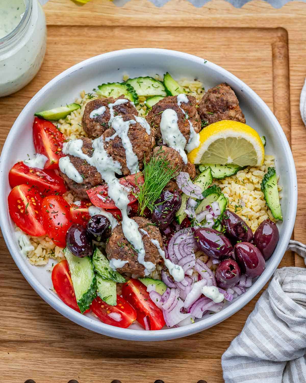 greek meatballs on a bowl served with bulgur and topped with kalamata olives and tzatziki sauce.