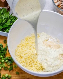 pouring the blended cheese and yogurt mixture over the shredded cheese in a bowl.
