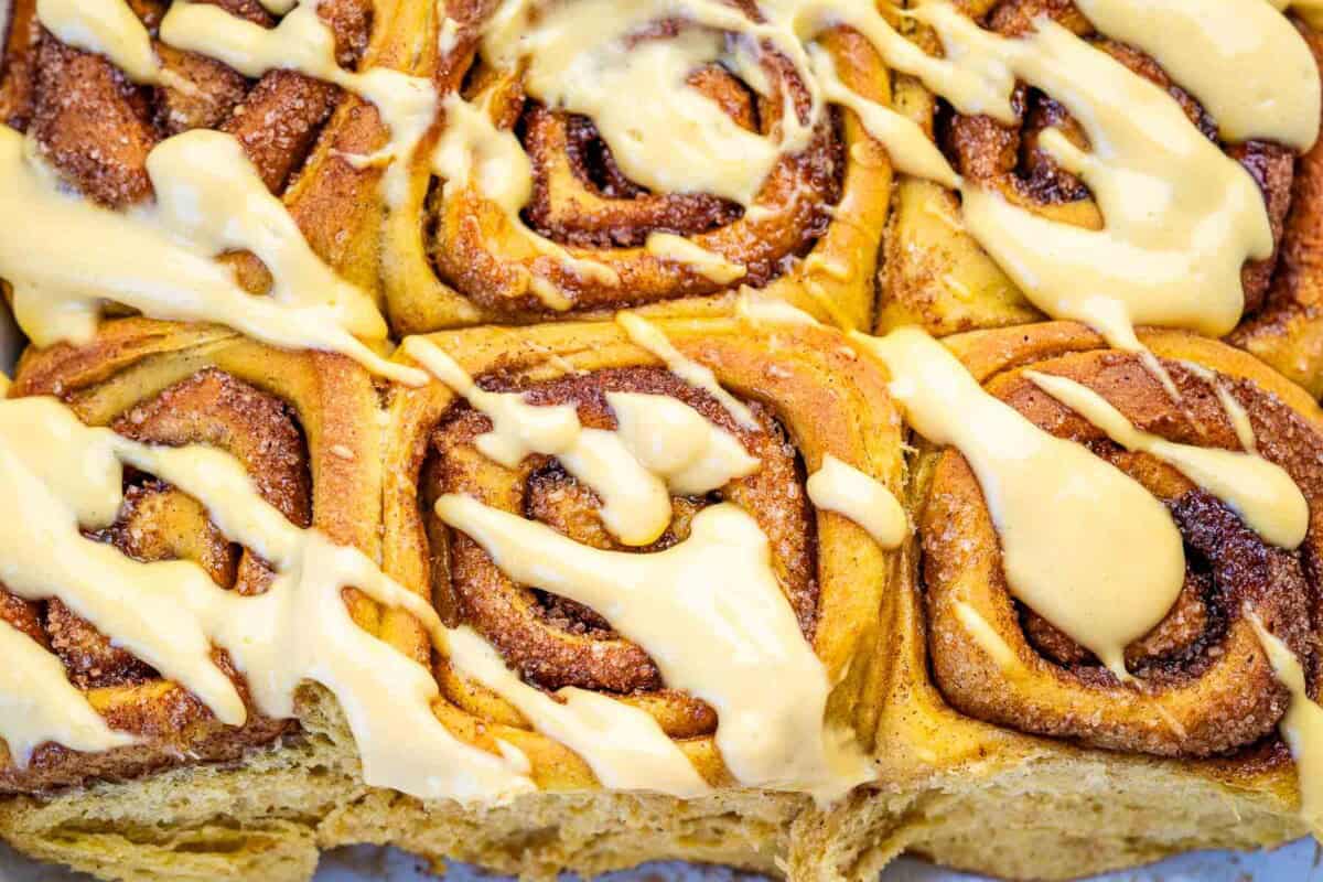 baked pumpkin cinnamon rolls in a dish with the yogurt pumpkin glaze.