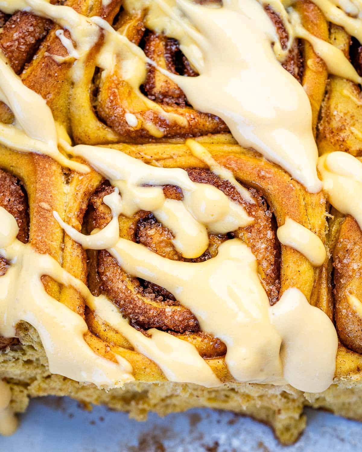 A pan of pumpkin cinnamon rolls drizzled with a maple yogurt glaze.