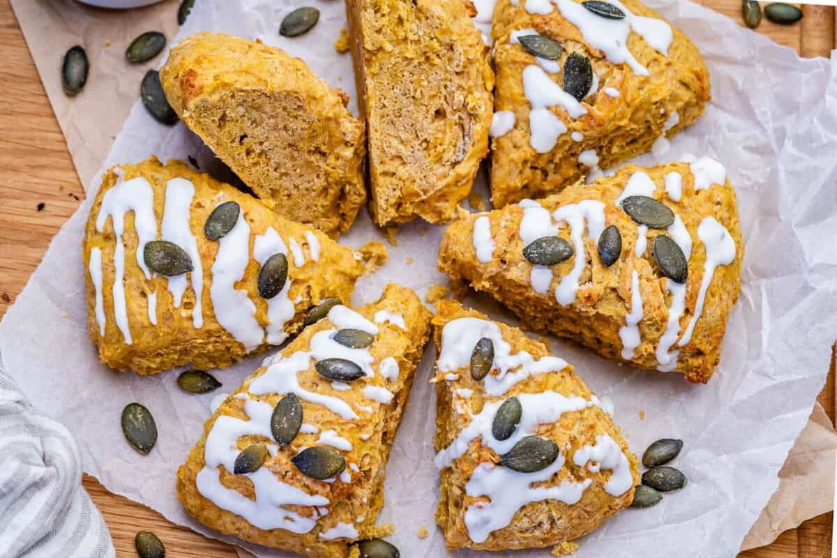 pumpkin scones laid out on a parchment paper. topped with yogurt glaze and pumpkin seeds. 
