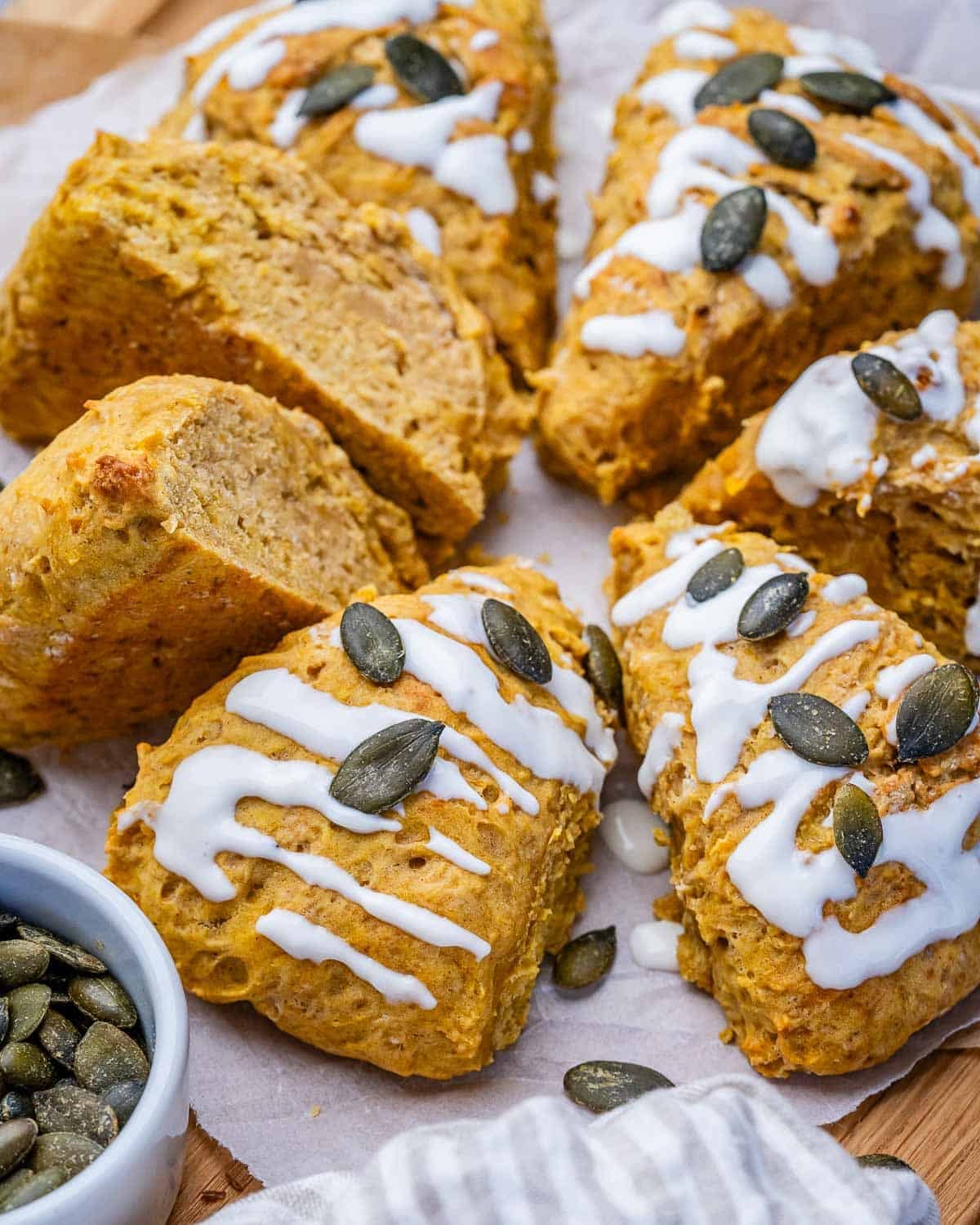 Pumpkin scones on parchment paper drizzled with glaze and sprinkled with pumpkin seeds.