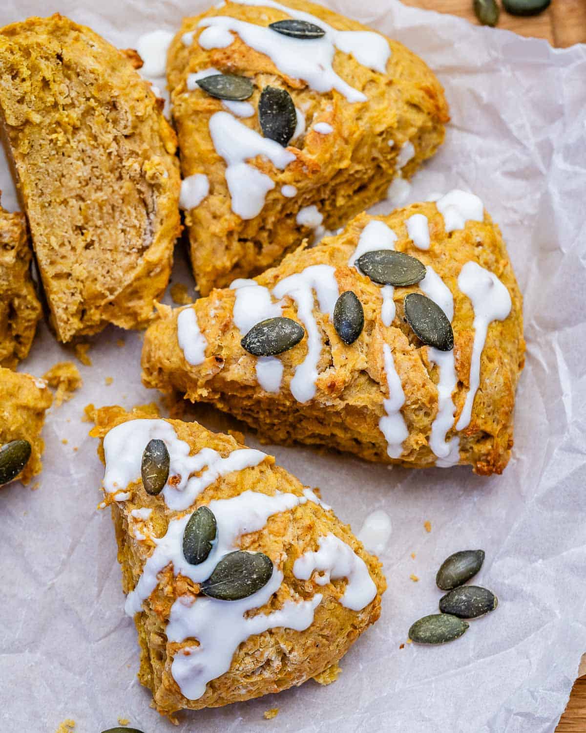 Glazed pumpkin scones with pumpkin seeds on parchment paper.