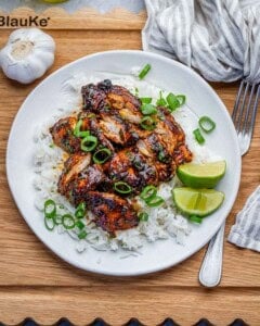 chicken thighs served over rice on a round plate.