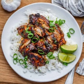 slow cooker chicken thighs served over rice on a plate and then topped with sliced green onions.