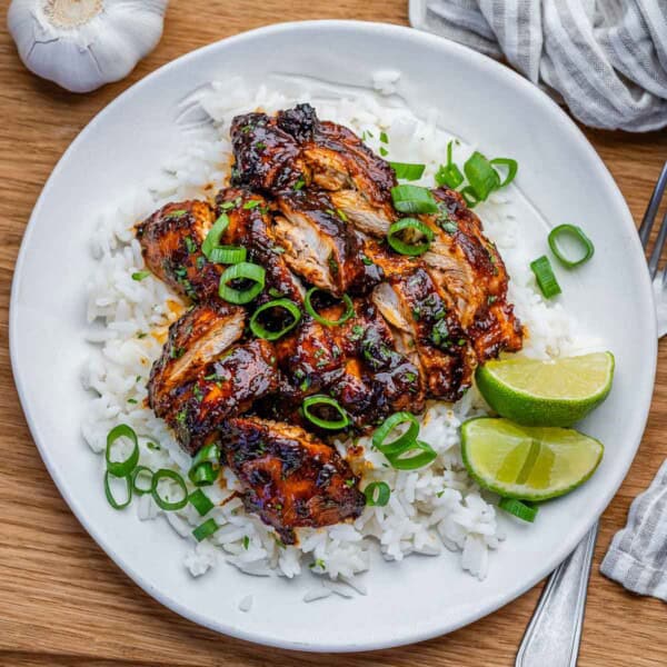 slow cooker chicken thighs served over rice on a plate and then topped with sliced green onions.