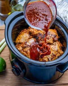 pouring chipotle sauce over the chicken thighs in the slow cooker.