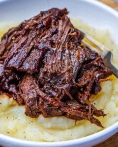 A white bowl of mashed potatoes topped with BBQ slow cooker chuck roast.
