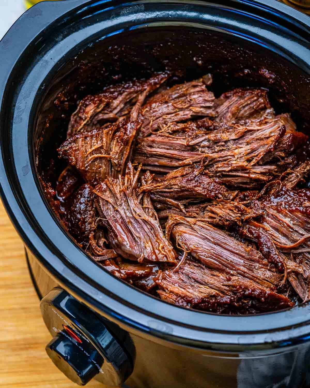 A slow cooker filled with shredded beef chuck roast.