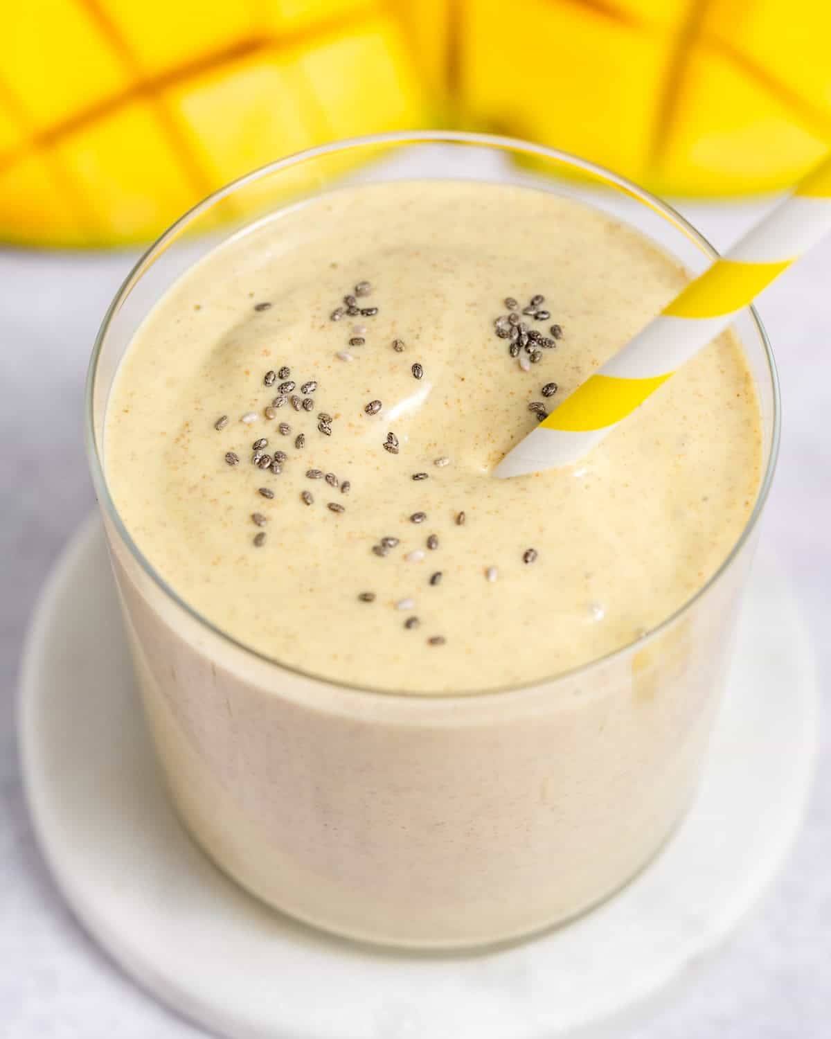 a glass jar with mango chia smoothie and a yellow straw in the cup.