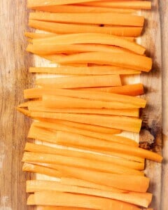 Carrots cut into sticks on a cutting board.