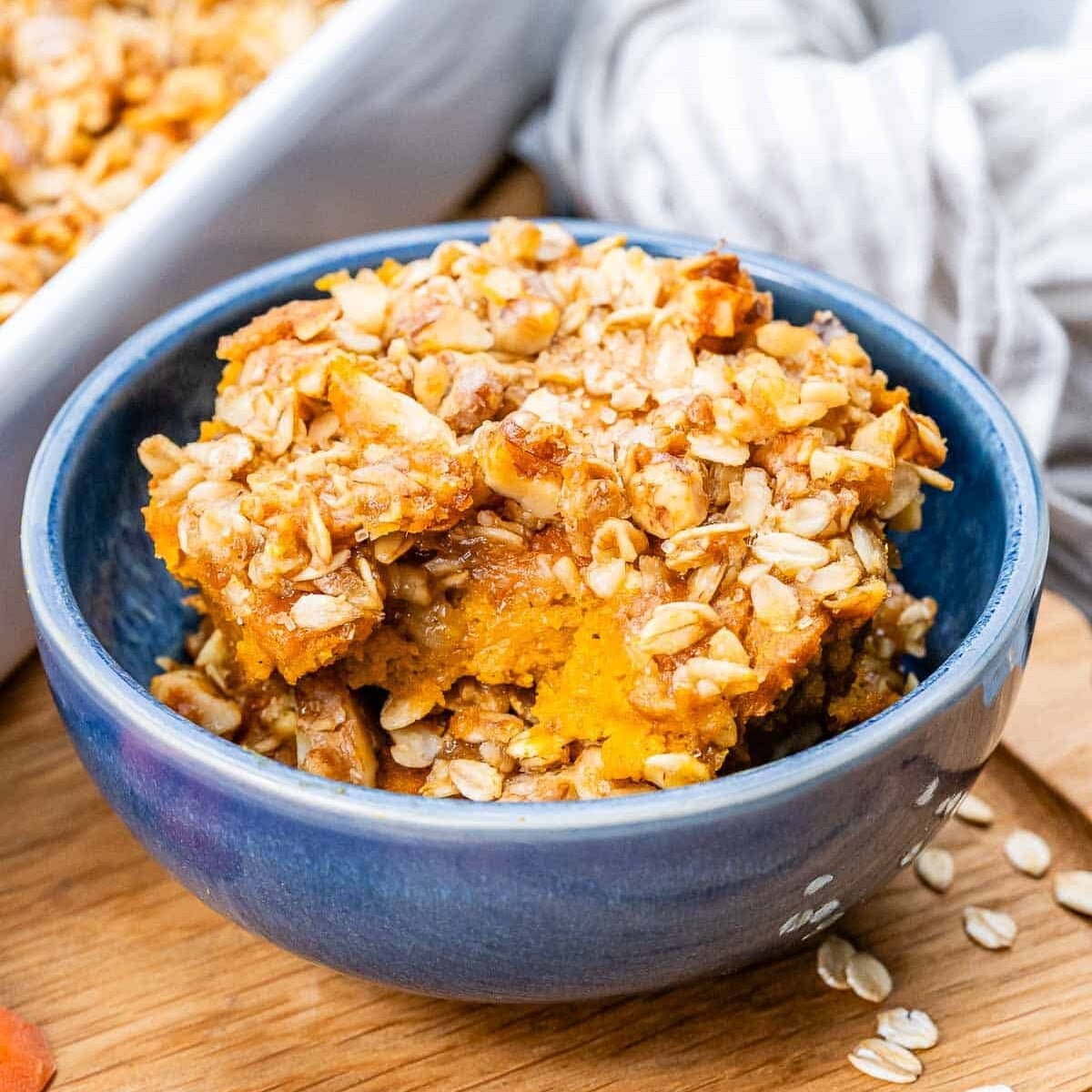 A blue bowl of carrot souffle on a wooden board.
