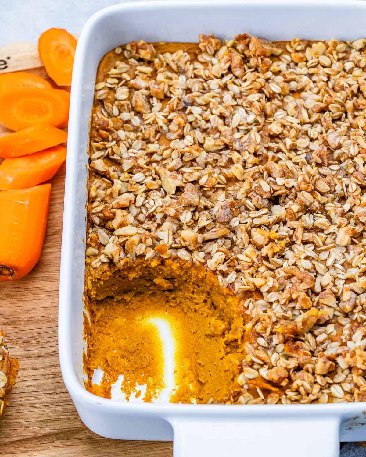 A white dish of carrot souffle topped with walnut oat crumble with a spoonful removed.