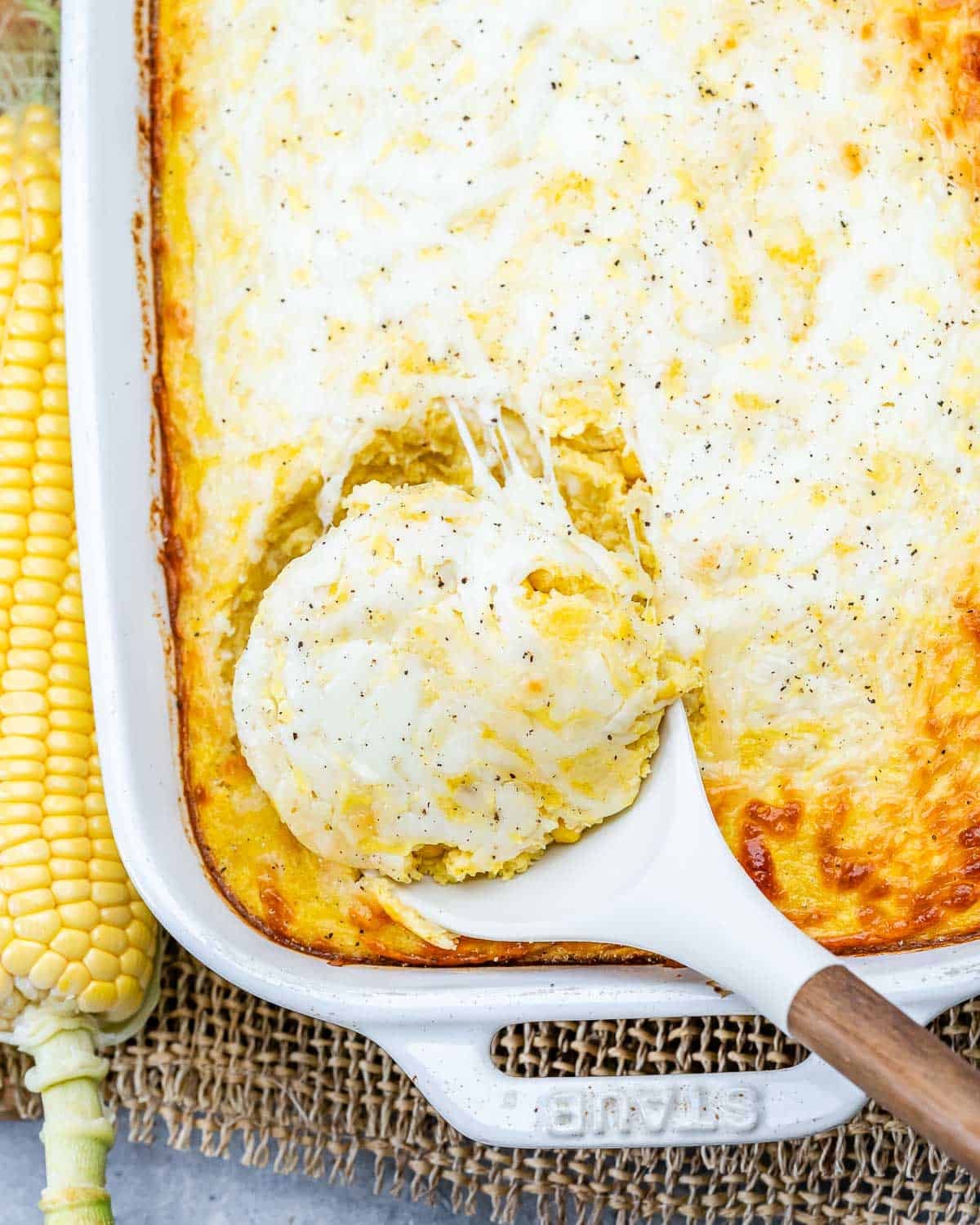 a dish with corn pudding casserole and a spoon grabbing a serving.
