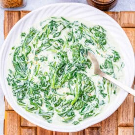 a round white bowl with creamed spinach with a spoon in the bowl.
