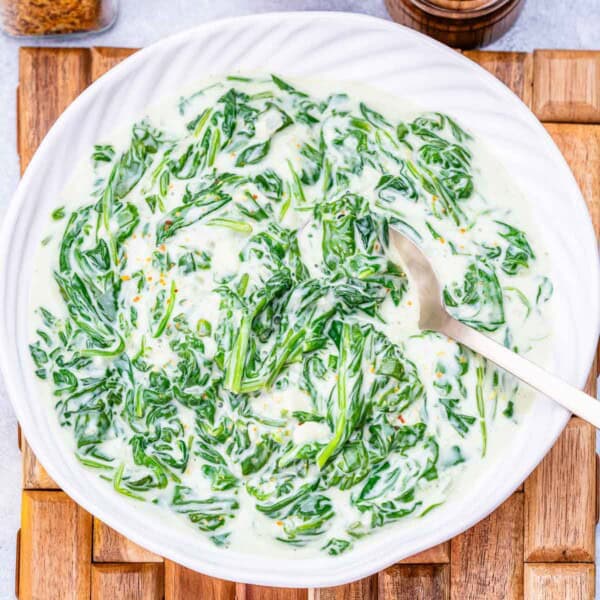 a round white bowl with creamed spinach with a spoon in the bowl.