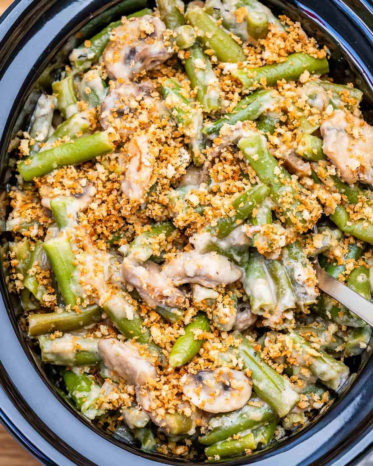 A slow cooker filled with green bean casserole topped with crispy panko breadcrumbs.
