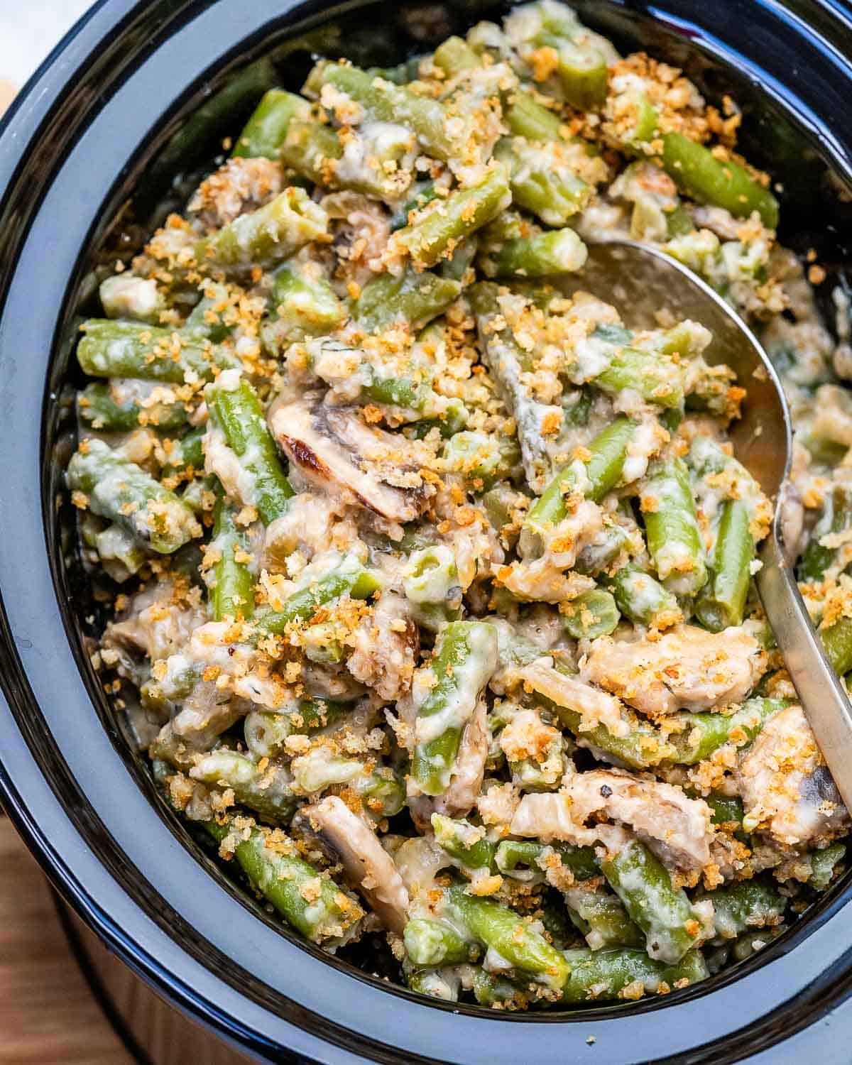 A crockpot filled with slow cooker green bean casserole and a serving spoon.