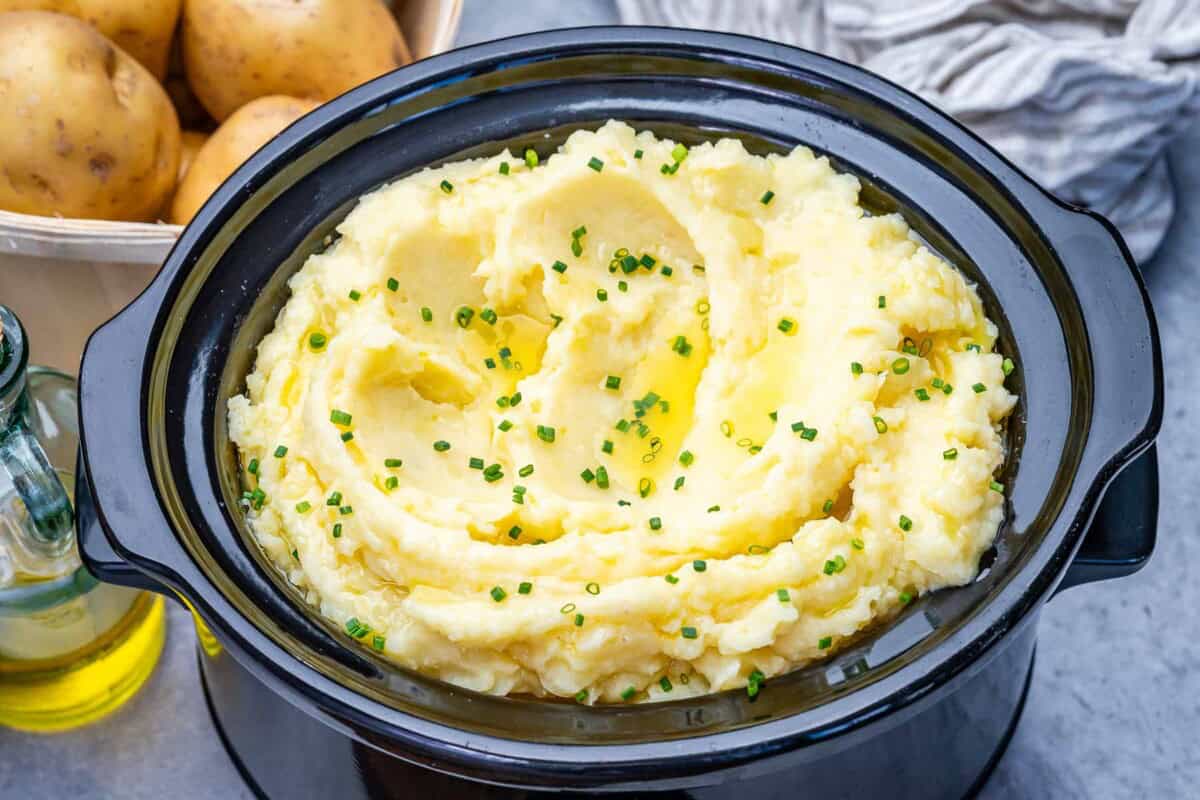 a slow cooker filled with mashed potatoes and topped with chives.