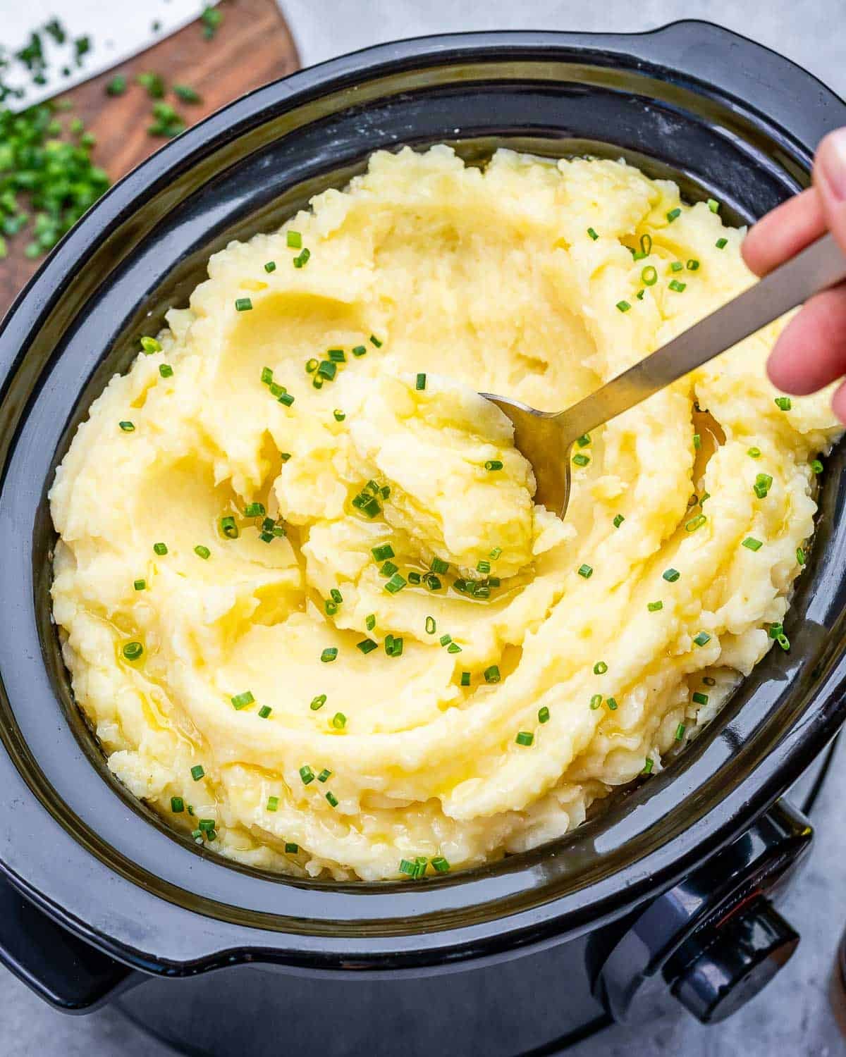 A spoon scooping up slow cooker mashed potatoes topped with chives.