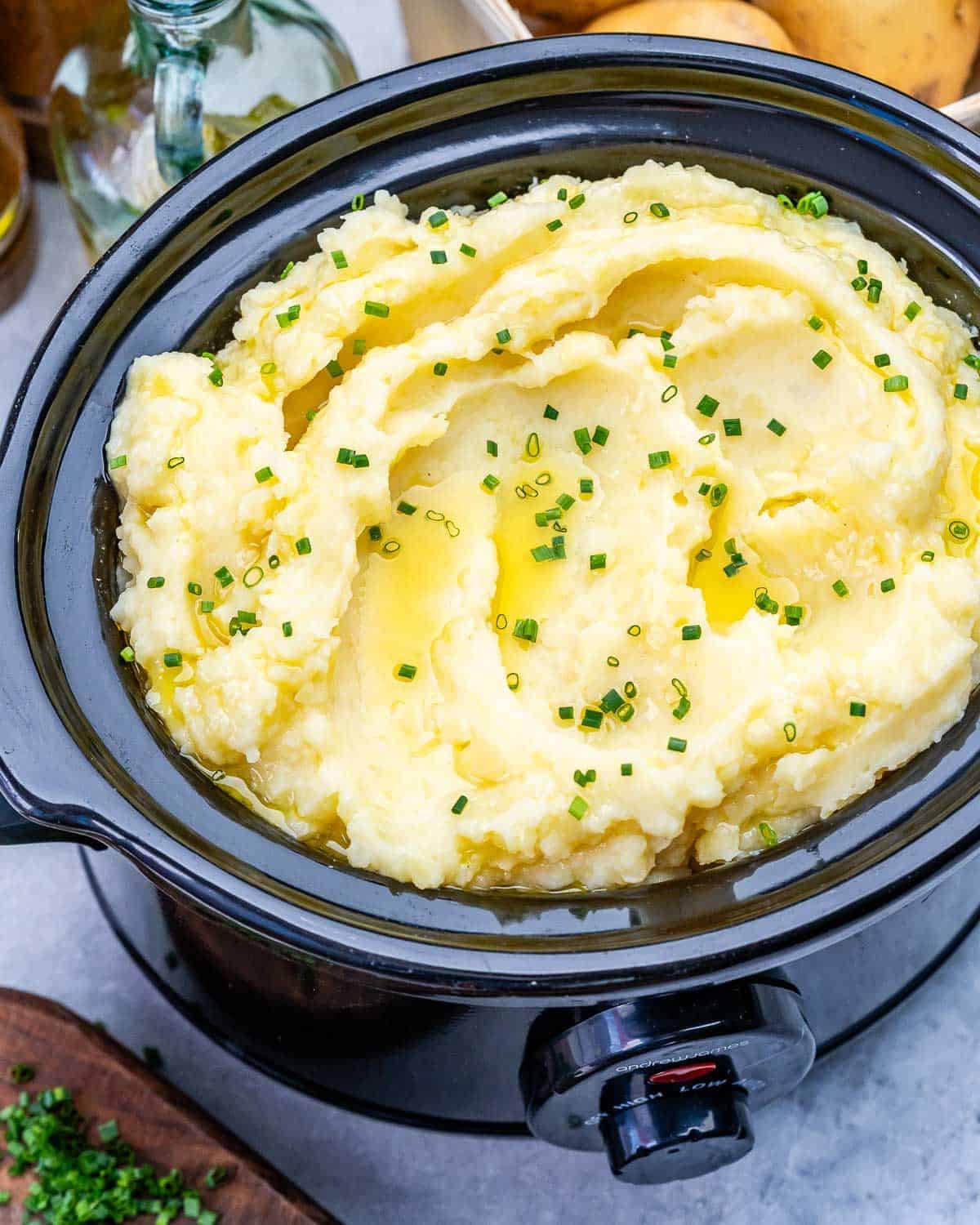 A slow cooker filled with creamy mashed potatoes topped with chives.