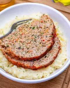 A white bowl with mashed potatoes and two slices or turkey meatloaf.