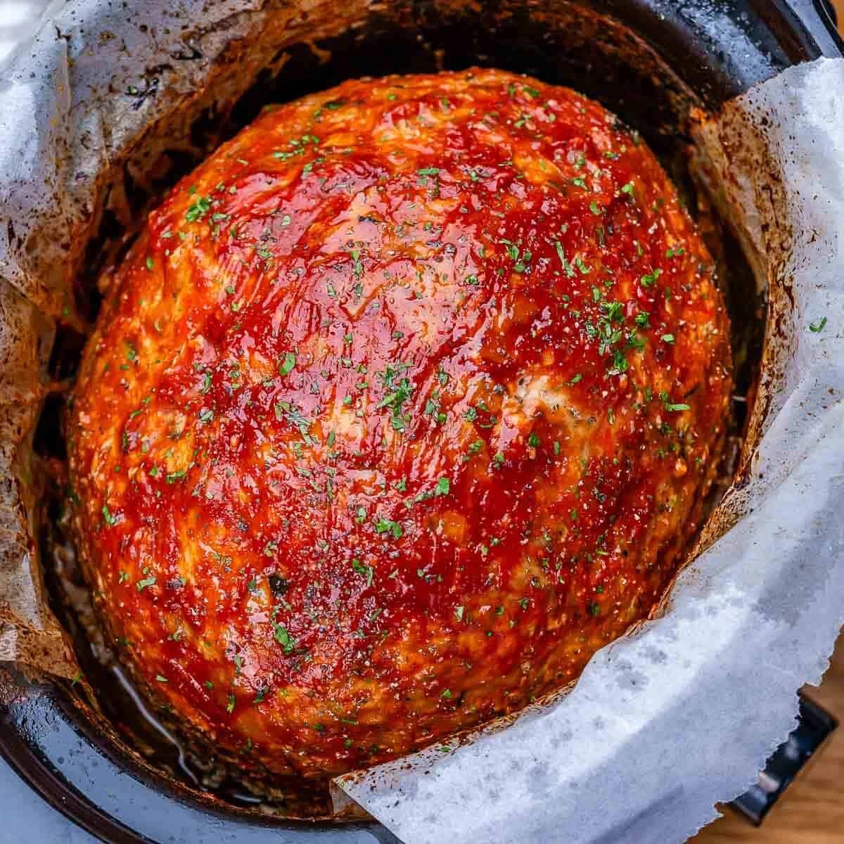 A slow cooker filled with an oval-shaped turkey meatloaf topped with ketchup glaze.