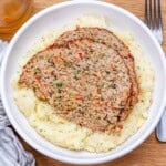 2 slices of meatloaf over mashed potatoes on a plate.