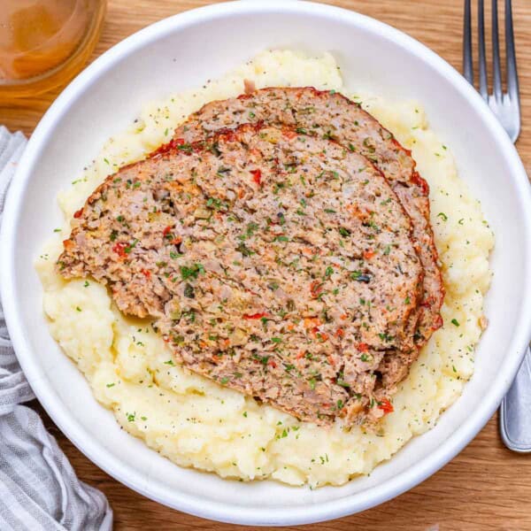 2 slices of meatloaf over mashed potatoes on a plate.
