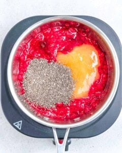 adding honey and chia seeds in a sauce pan with mashed raspberries.
