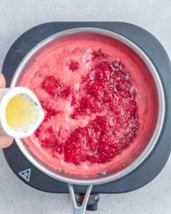 adding lemon juice to cooking mashed raspberries in a pan.