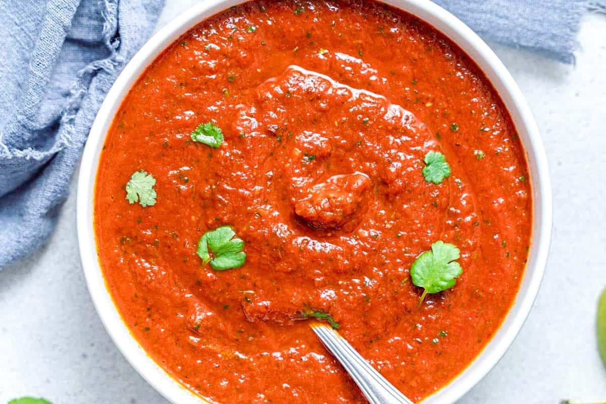 ranchero sauce in a bowl with spoon in a bowl and a few cilantro leaves over the sauce.