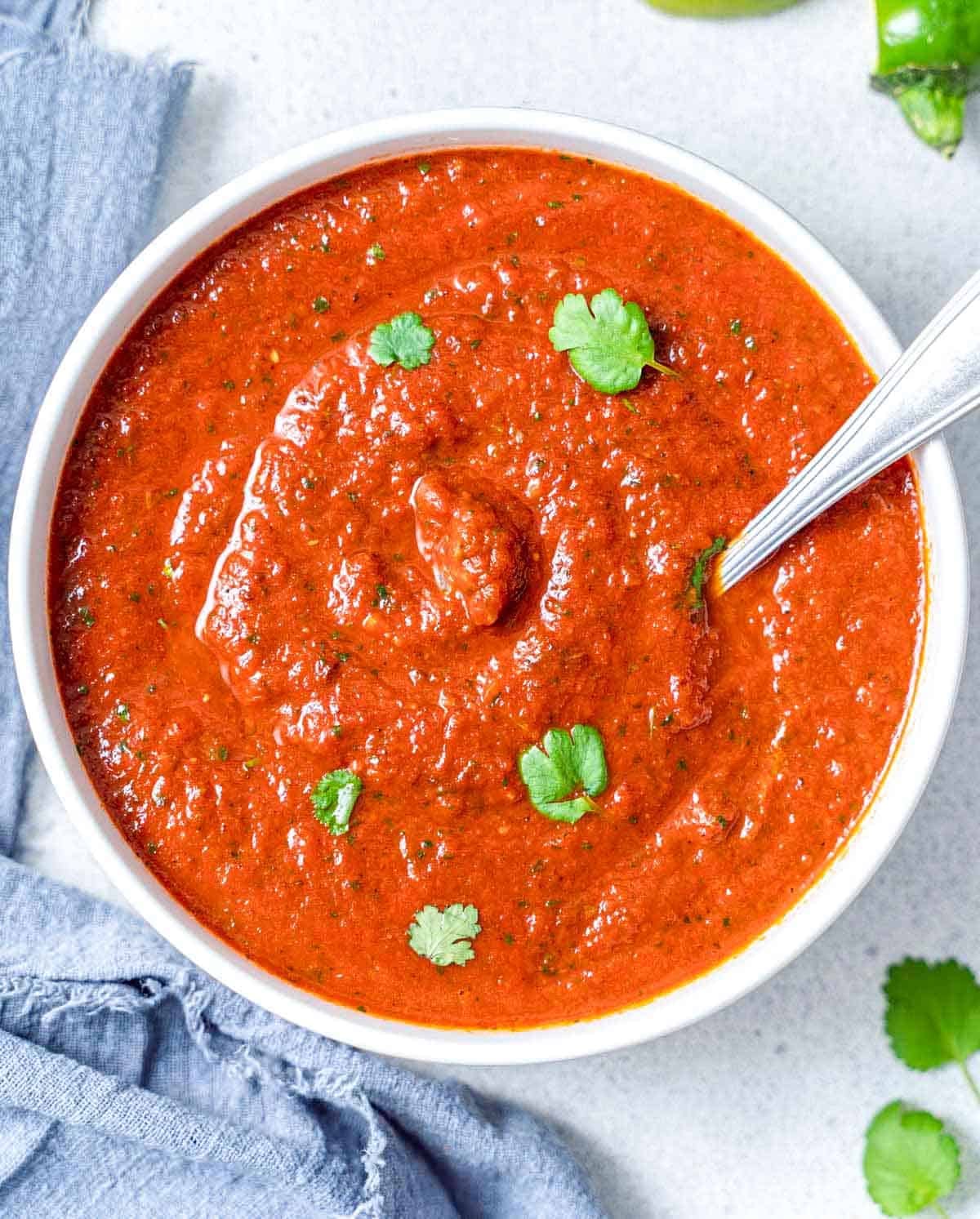ranchero sauce in a bowl topped with cilantro and a spoon in the bowl.