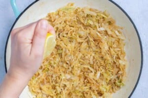 adding lemon juice to the sauteed cabbage in a pan.